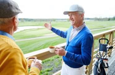 Two aged men with tea having talk in outdoor cafe about new area for playing golf